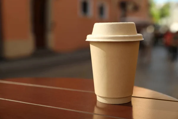 Cardboard takeaway coffee cup with lid on wooden table in city, space for text