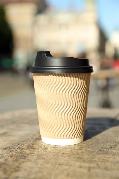 Cardboard takeaway coffee cup with plastic lid on wooden table in city