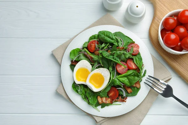 Delicious salad with boiled egg, bacon and tomatoes served on white wooden table, flat lay