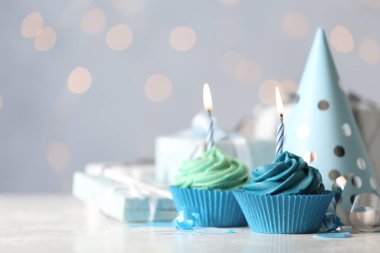 Delicious birthday cupcakes with cream and burning candles on white table. Space for text