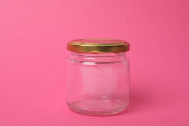 Closed empty glass jar on pink background