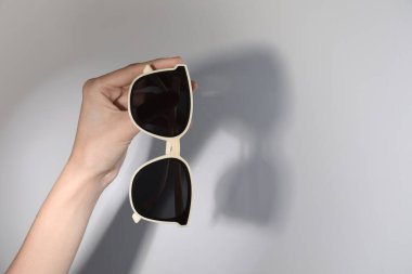 Woman holding stylish sunglasses on light background, closeup. Space for text