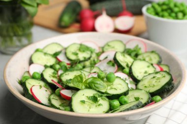 Appetizing salad with cucumbers, radish and pea in bowl on table, closeup
