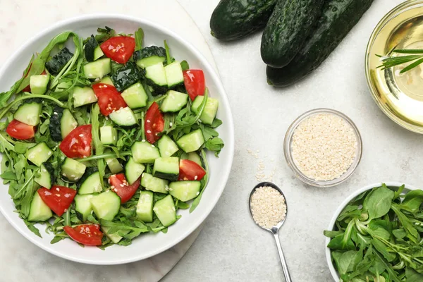 Delicious salad with cucumbers, tomatoes and sesame in bowl served on light table, flat lay