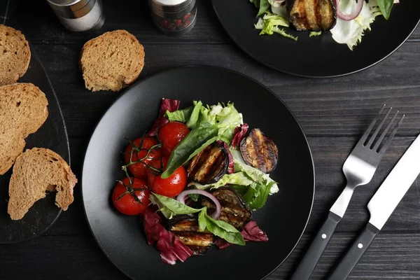Delicious salad with roasted eggplant and basil served on black wooden table, flat lay