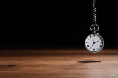 Beautiful vintage pocket watch with silver chain on black background above wooden table, space for text. Hypnosis session