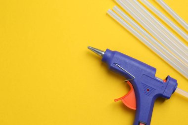 Blue glue gun and sticks on yellow background, flat lay. Space for text