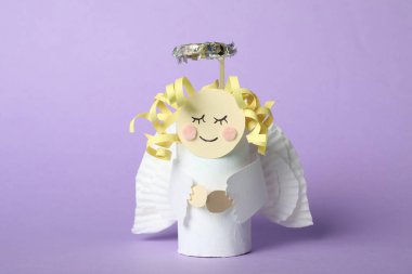Toy angel made of toilet paper hub on lilac background