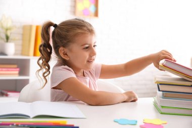 Kitapları olan sevimli küçük bir kız masada ödev yapıyor.