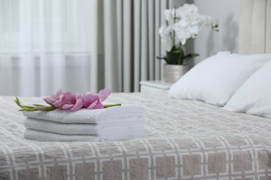 Stack of clean towels and gladiolus flowers on bed indoors, space for text