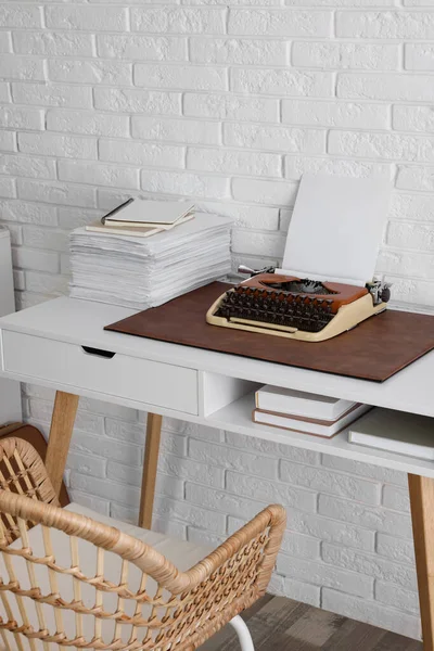 Comfortable writer's workplace with typewriter on desk near white brick wall