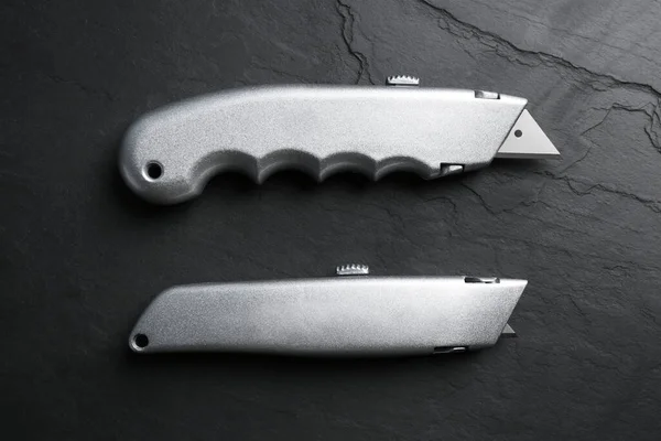 Two utility knives on black table, flat lay