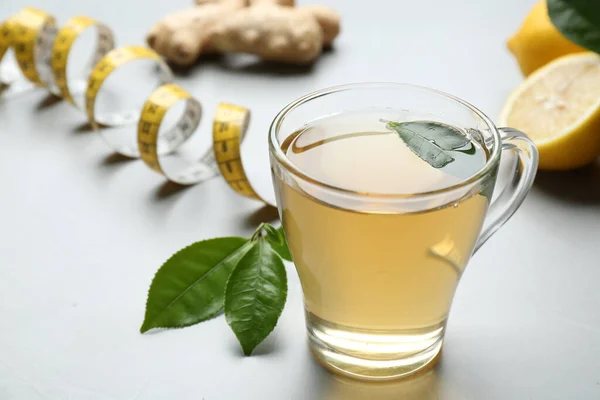 Herbal diet tea, lemon, ginger and measuring tape on light table