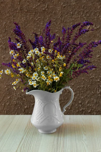 Beautiful bouquet with field flowers in jug on white wooden table