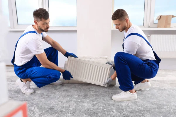 Professional plumbers with new heating radiator in room