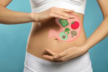 Woman with image of stomach full of food drawn on her belly against light blue background, closeup. Healthy eating habits