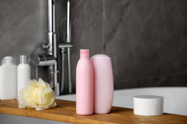 Ahşap banyo tepsisi, şampuan, saç kremi ve küvetteki diğer tuvalet malzemeleri.