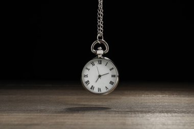 Beautiful vintage pocket watch with silver chain on black background above wooden table. Hypnosis session