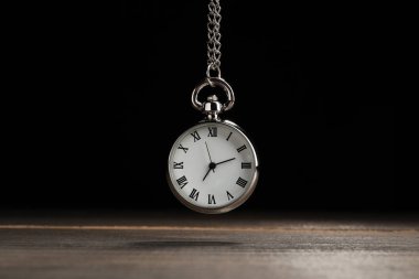 Beautiful vintage pocket watch with silver chain on black background above wooden table. Hypnosis session