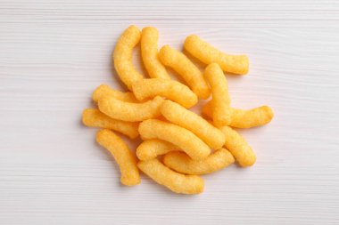Heap of tasty cheesy corn puffs on white wooden table, flat lay