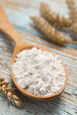 Spoon of wheat flour on light wooden table, closeup