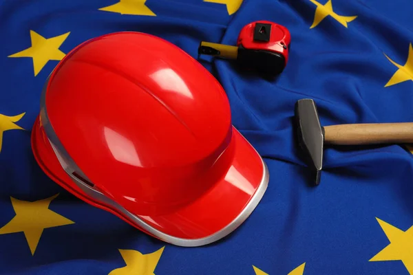 Red hard hat, measuring tape and hammer on flag of European Union