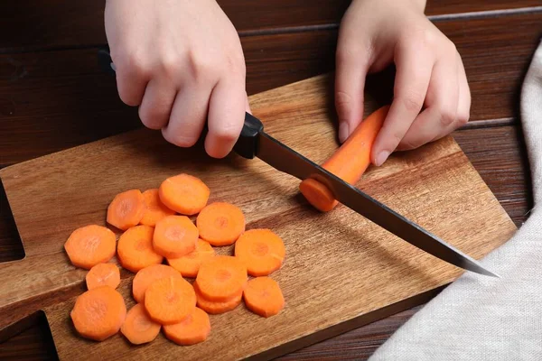 Woman Cutting Tasty Carrot Brown Wooden Table Closeup — Stok Foto