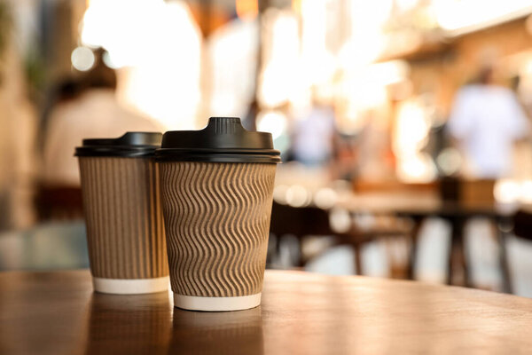 Cardboard takeaway coffee cups with plastic lids on wooden table in city, space for text