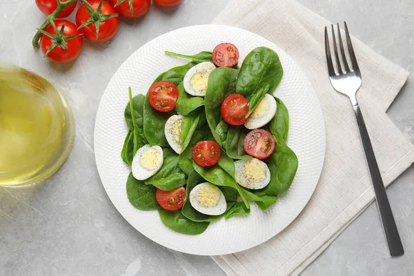 Delicious salad with boiled eggs, tomatoes and spinach served on light grey table, flat lay