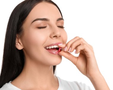 Beyaz arka planda vitamin kapsülü alan genç bir kadın.