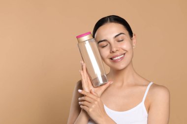Young woman with bottle of micellar water on beige background, space for text