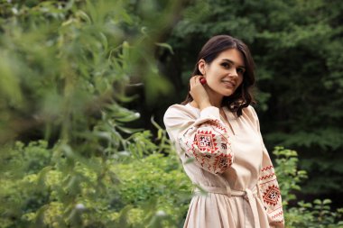 Beautiful woman wearing embroidered dress in countryside, space for text. Ukrainian national clothes