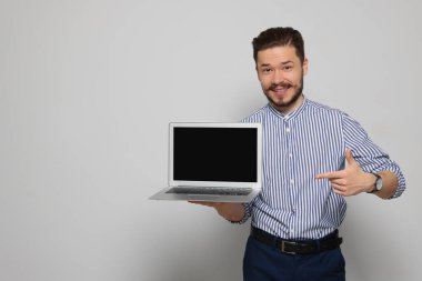 Emotional man pointing at laptop on light grey background. Space for text