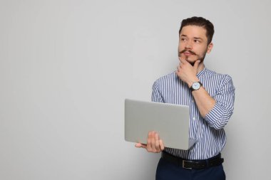 Pensive man using laptop on light grey background. Space for text