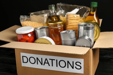 Donation box with food on black table, closeup
