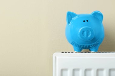 Piggy bank on heating radiator against beige background, space for text