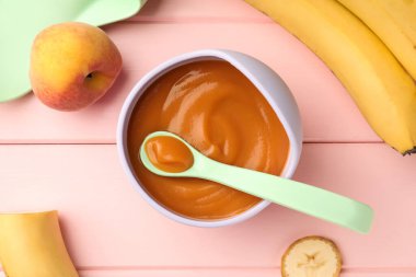 Healthy baby food in bowl and fresh fruits on pink wooden table, flat lay