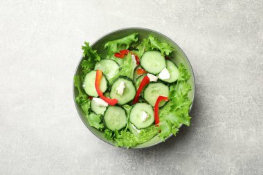 Delicious salad with cucumbers, red bell pepper and feta cheese in bowl on light grey table, top view
