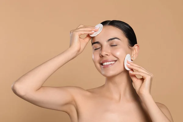 Young woman using cotton pads with micellar water on beige background