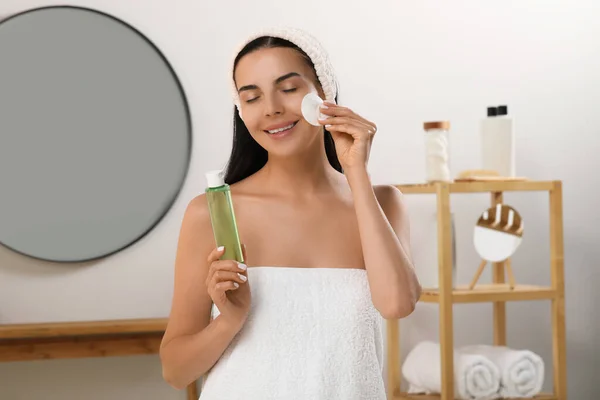 Young woman using cotton pad with micellar water indoors