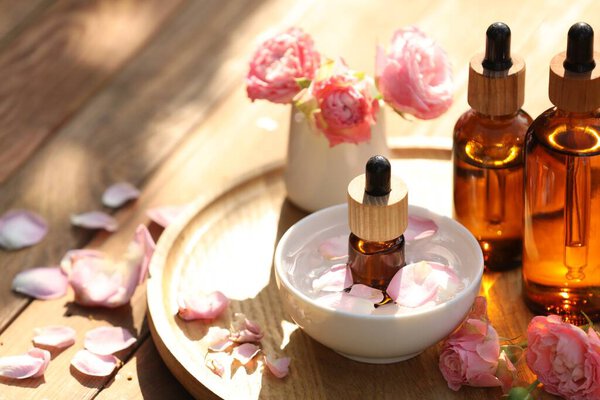 Бутылки розового эфирного масла и цветы на деревянном столе, место для текста
