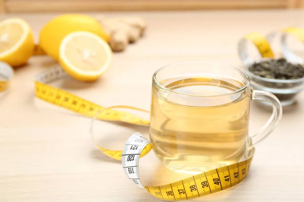 Diet herbal tea and measuring tape on wooden table, space for text