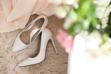 Pair of white high heel shoes and wedding dress on fuzzy rug, top view