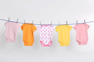 Colorful baby onesies drying on laundry line against light background