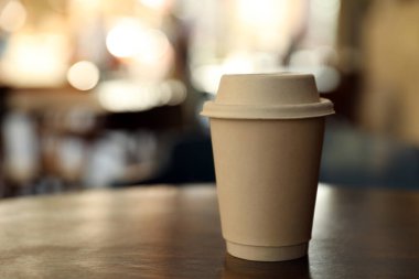 Cardboard takeaway coffee cup with lid on wooden table in outdoor cafe, space for text