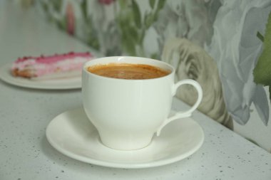 Cup of delicious aromatic coffee and eclair on white table indoors, closeup