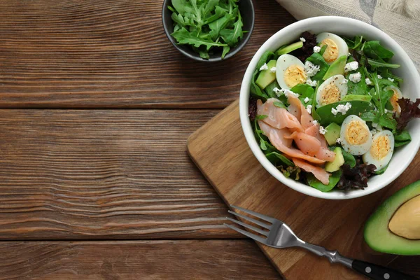 Delicious salad with boiled eggs, salmon and cheese served on wooden table, flat lay. Space for text
