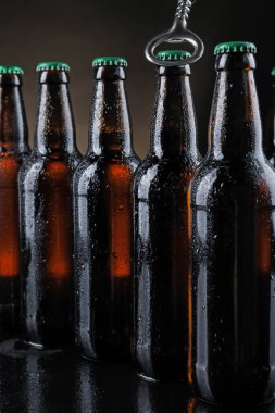 Koyu arkaplanda bira şişesi açılıyor, yakın plan.