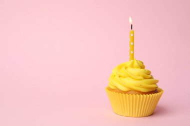Delicious birthday cupcake with yellow cream and burning candle on pink background. Space for text