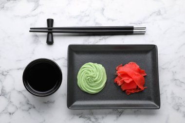 Swirl of wasabi paste, pickled ginger, soy sauce and chopsticks on white marble table, flat lay